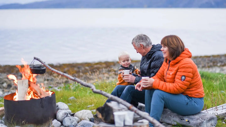 En dame i oransje boblejakke, en mann i en grå boblejakke og et lite barn sitter rundt et bål i fjæra og griller. Artikkelen handler om å ta Vitamin C