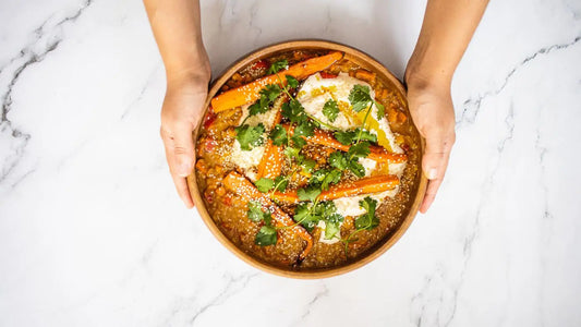 To hender holder et fat med en vegansk rett på en marmorbakgrunn.