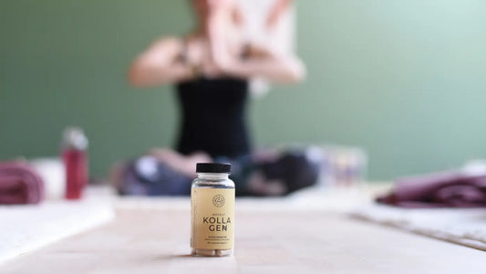 En dame kledt i svart sitter i lotusposisjon på enden av en yogamatte, hun er ufokusert mens det i forgrunnen står en boks med kosttilskudd i fokus